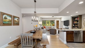 Une cuisine spacieuse avec une table à manger en bois, des bancs et un îlot central intégré, doté d’un évier et d’un lave-vaisselle.