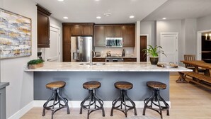Une cuisine moderne dotée d’un îlot central, de tabourets de bar, d ’appareils électroménagers en acier inoxydable et d’un coin repas avec une table et des chaises en bois.