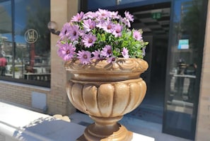 A large, ornate flower pot with purple flowers on a sidewalk in front of a building.