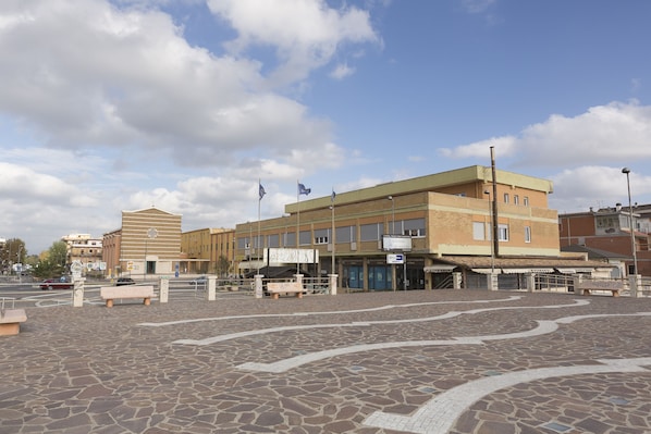 A public square with a paved area, benches, and a building with a signboard.