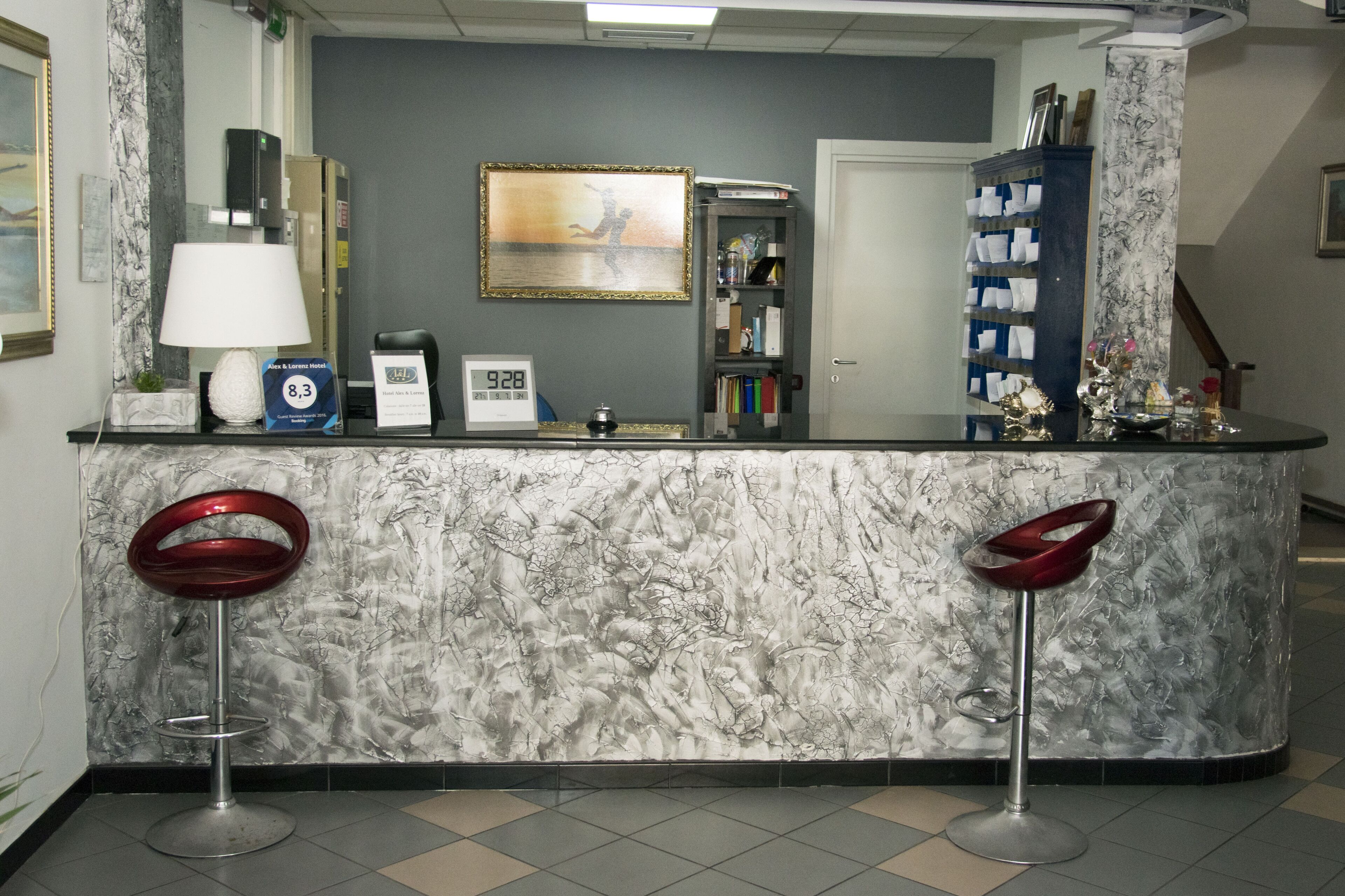 A reception area with a marble counter, two red bar stools, a clock, a framed picture, and a bookshelf.