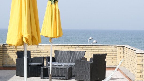 Una terraza con mobiliario de mimbre y sombrillas amarillas, con vistas al mar.