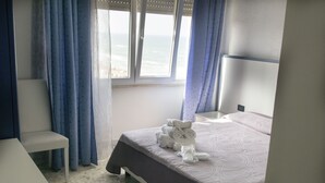 Un dormitorio con cama, una silla, un ventanal con cortinas y vista al mar.