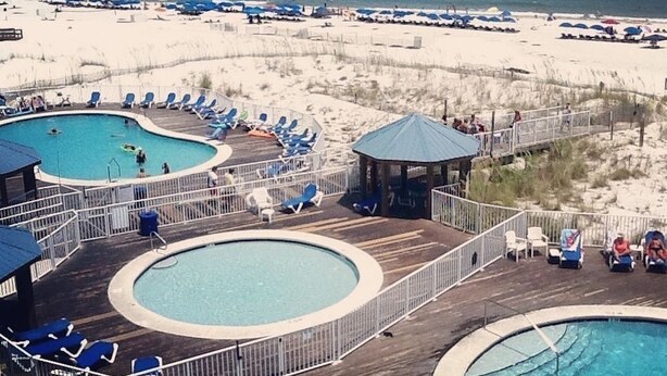 A pool area with two circular pools and lounge chairs, surrounded by a wooden deck and a beach in the background. - Perfect for quite Beach Lovers. Four pools.Fall/Off Season Week-Month Specials!
 (Orange Beach)
