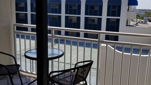 A balcony with two chairs and a small table, overlooking a building with arched windows and a blue awning. - Perfect for quite Beach Lovers. Four pools.Fall/Off Season Week-Month Specials!
 (Orange Beach)