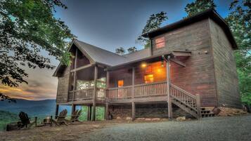 A wooden cabin with a balcony, stone foundation, and a view of the water.