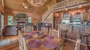 Ein rustikales Blockhaus-Interieur mit Essbereich, Kamin, Küche mit Steinwand und Treppe.