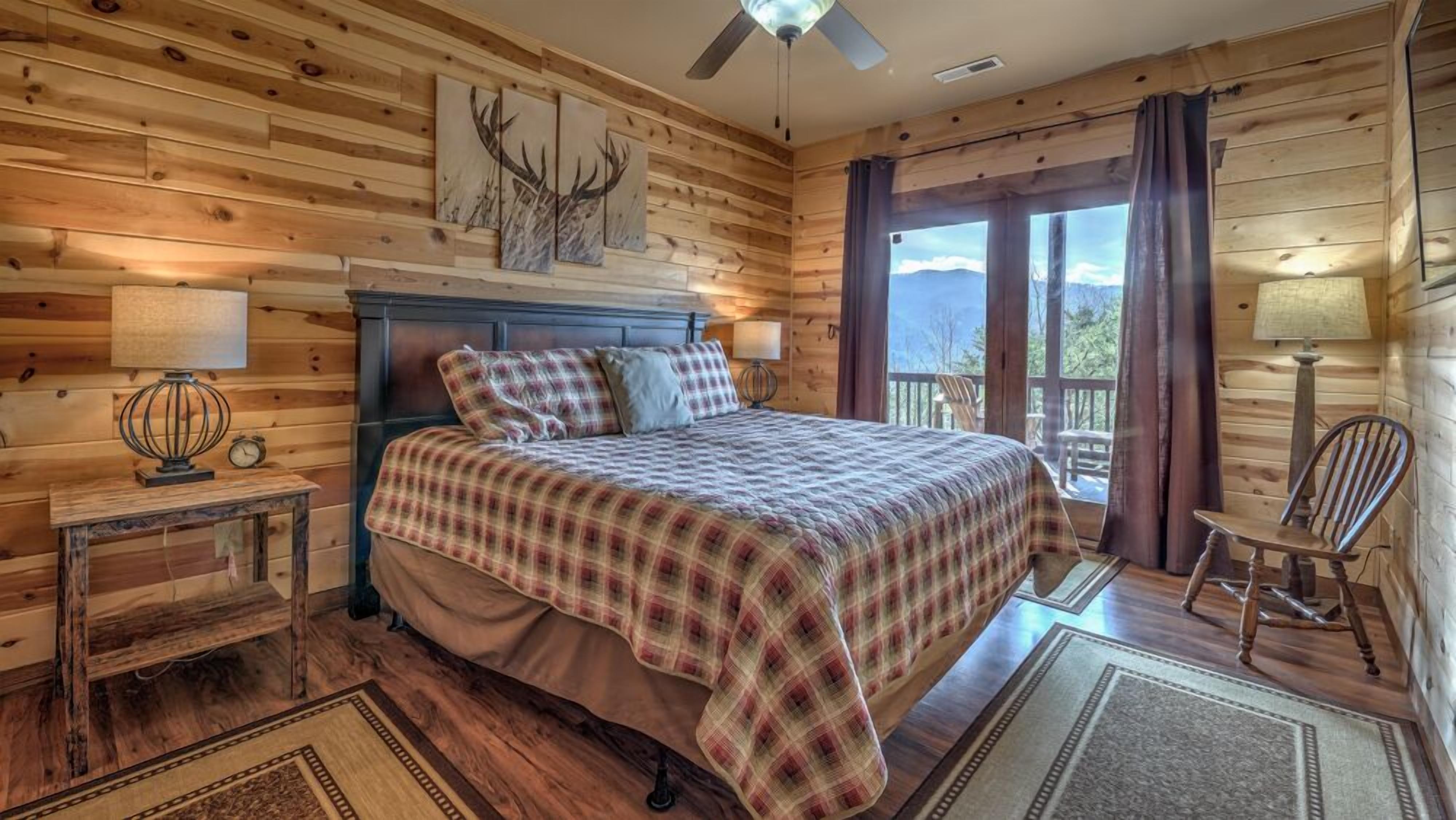 Une chambre confortable, aménagée dans une cabane en bois, avec un lit, deux tables de chevet, un ventilateur de plafond et une vue sur l’extérieur.