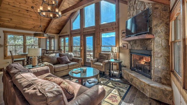 A spacious living room with a stone fireplace, leather sofas, and large windows offering mountain views.