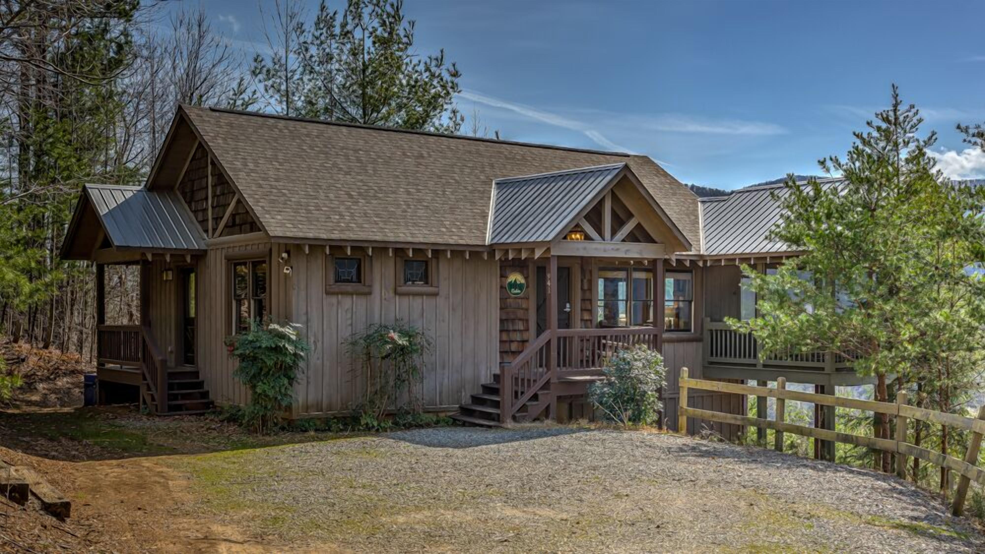 A wooden cabin with a porch, a staircase, and a fenced area.