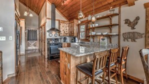 A rustic kitchen with wooden cabinets, a large island with bar stools, and a hanging light fixture.