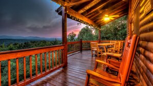 Una terraza de madera con vistas a montañas y un atardecer.