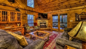 L’intérieur chaleureux d’un chalet avec une cheminée en pierre, des meubles en bois et une grande fenêtre donnant sur la forêt.