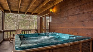Une terrasse en bois avec un jacuzzi, des chaises en bois et un mur de pierre en arrière-plan.