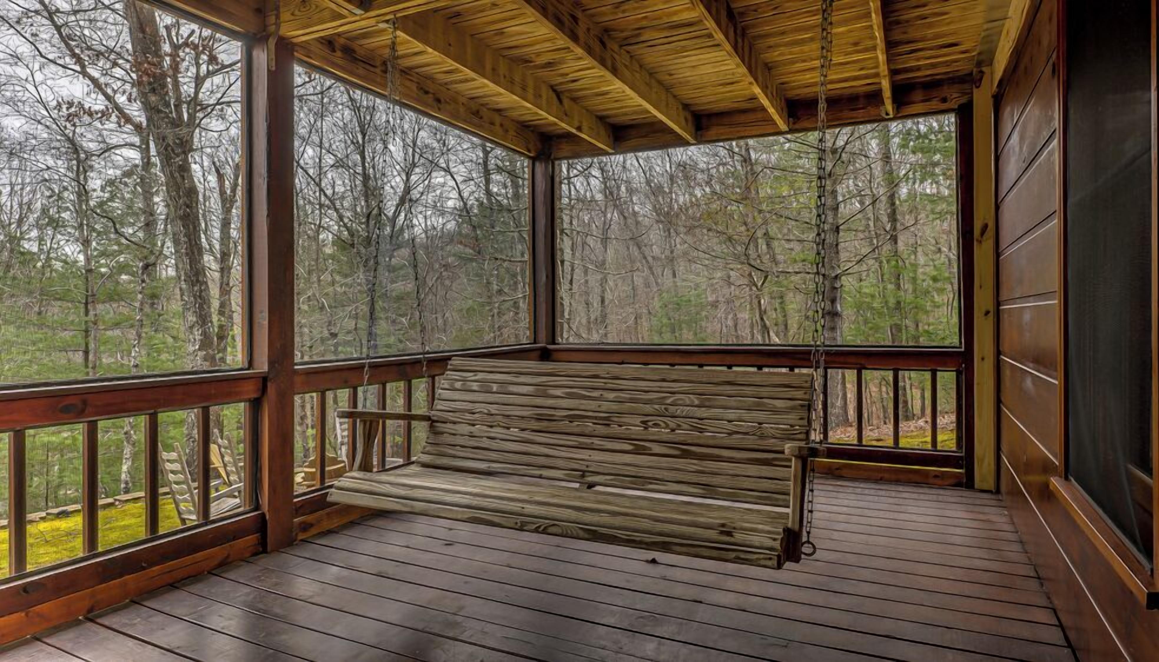 A wooden deck with a bench, surrounded by trees.