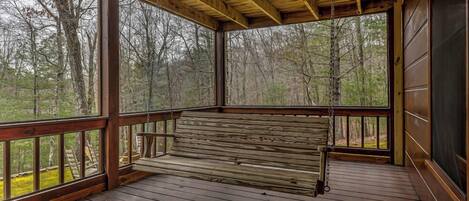 A wooden deck with a bench, surrounded by trees.