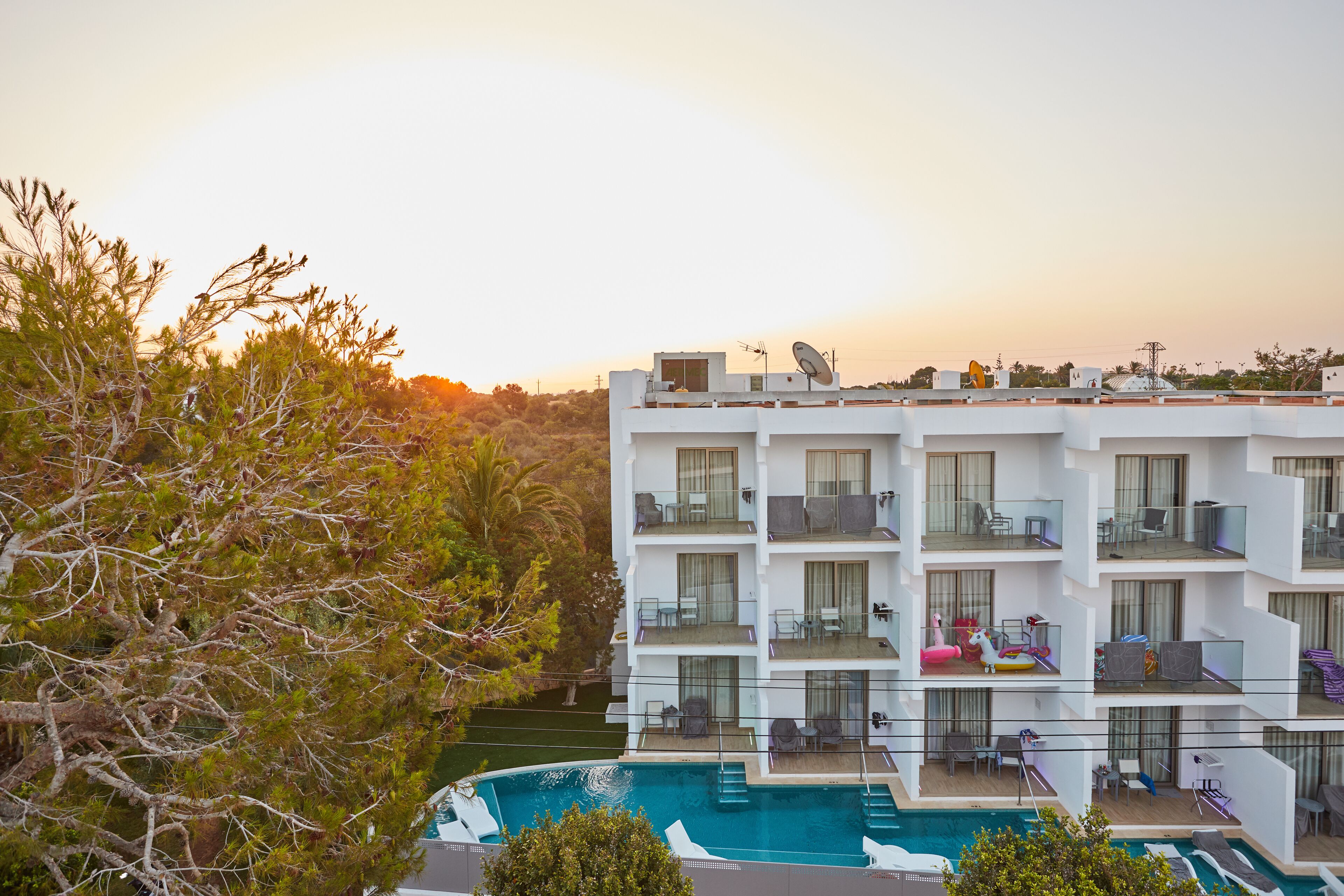 A modern hotel with multiple balconies, a swimming pool, and lush greenery.