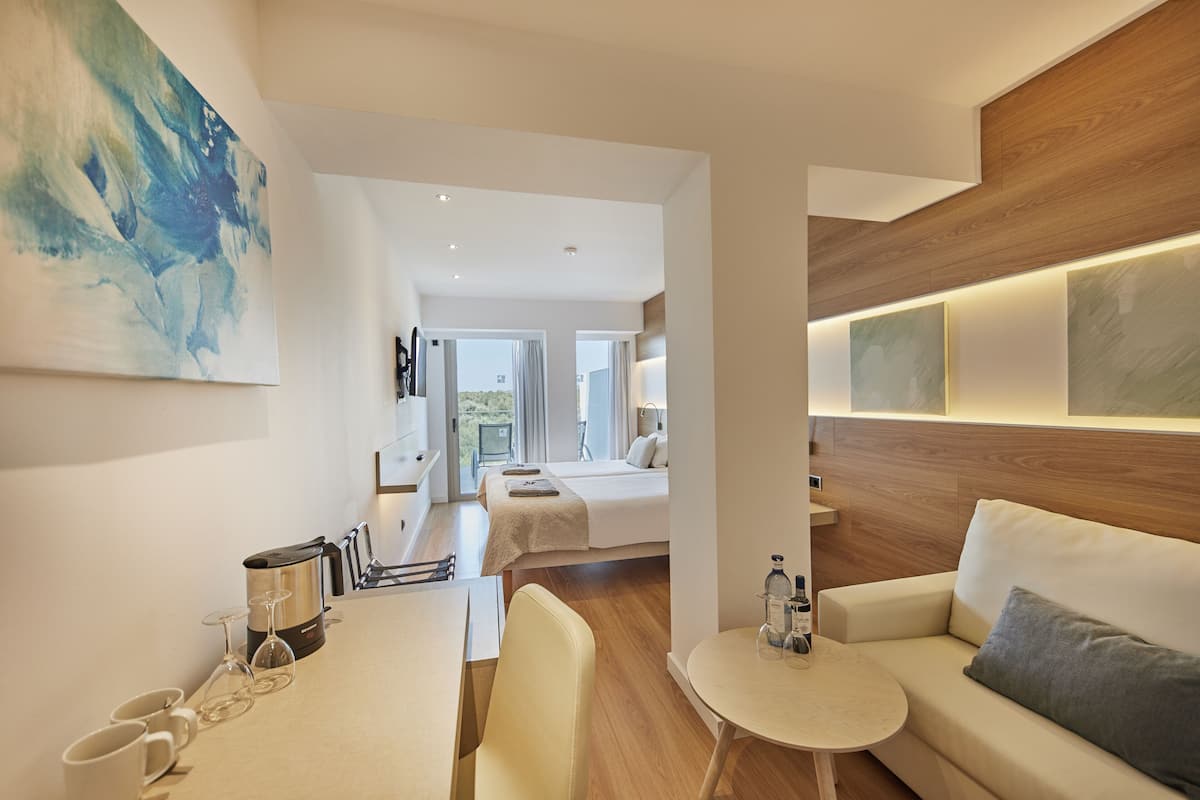 A modern hotel room with a bed, a sofa, a small table, and a coffee machine.