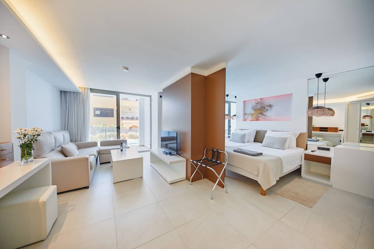 A modern hotel room with a sofa, a bed, a TV, and a desk.