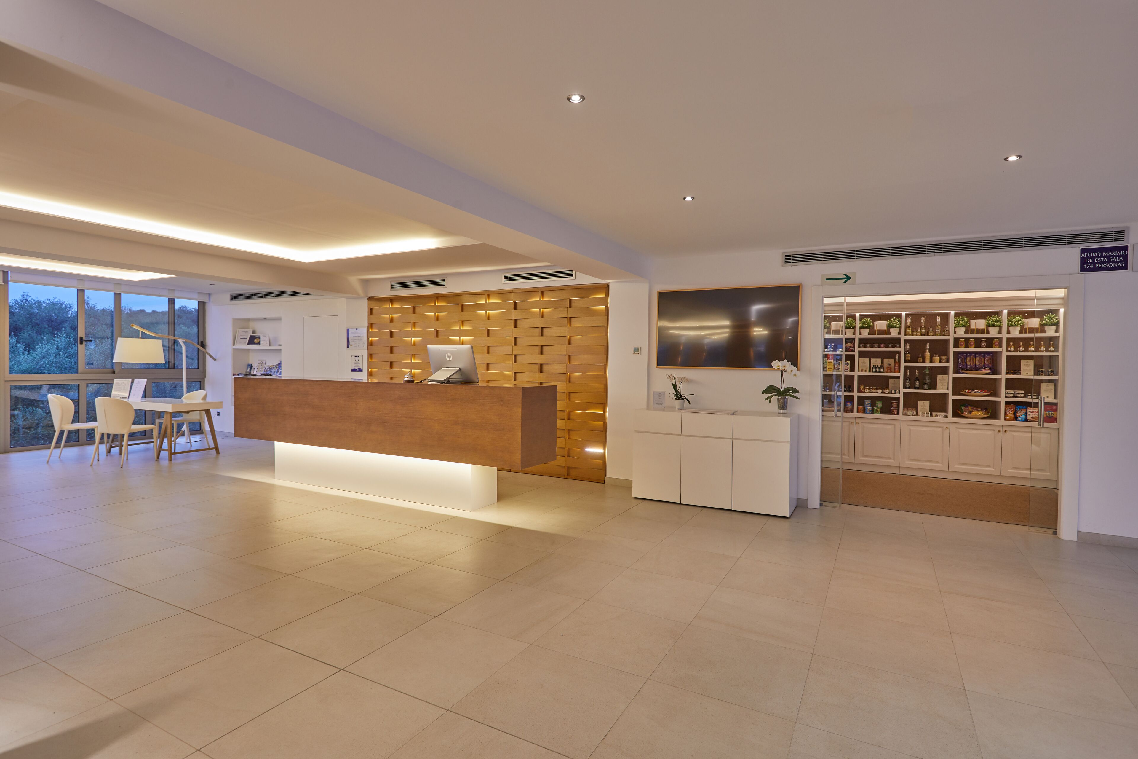 A modern reception area with a wooden reception desk, a white counter, and a display of products. There is a seating area with chairs and a table.