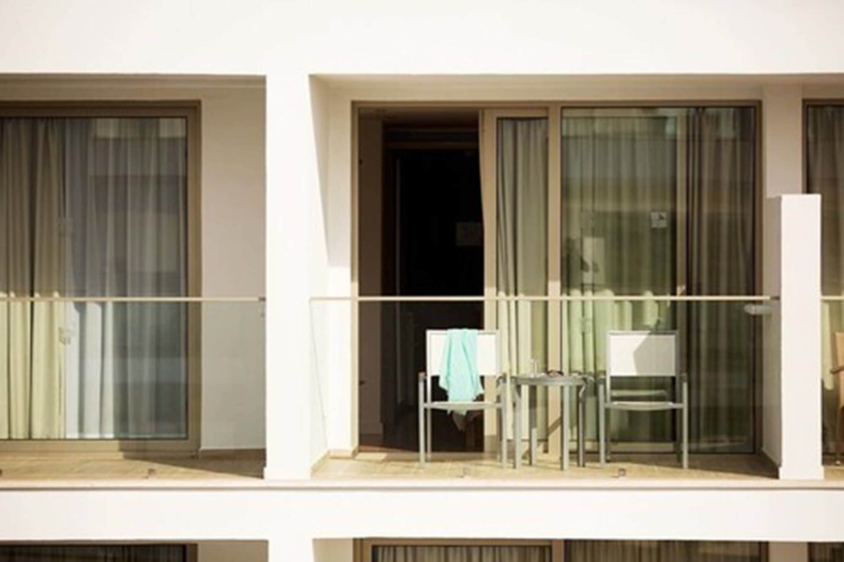 Un balcon avec une chaise et une table, une porte-fenêtre coulissante et une vue sur la rue.