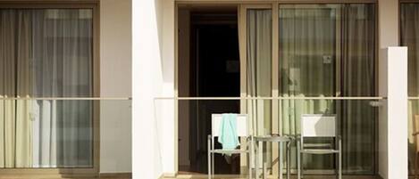 A balcony with a chair and a table, a sliding glass door, and a view of the street.
