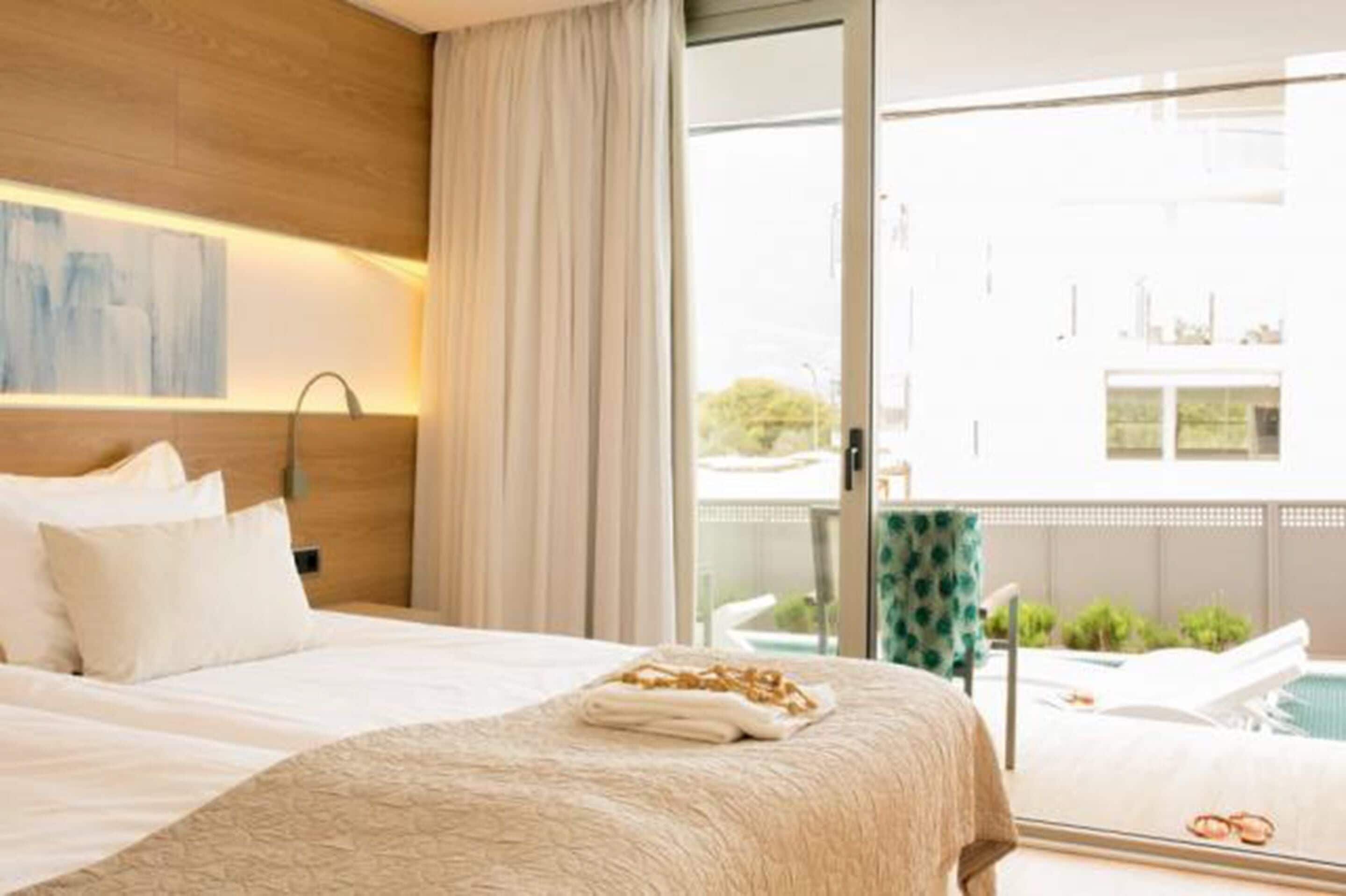 A hotel room with a bed, a view of the outdoors, and a balcony with a pool.