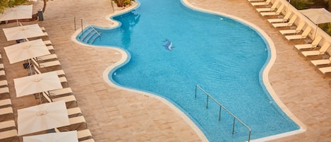 A swimming pool with a wavy edge, surrounded by lounge chairs and umbrellas.