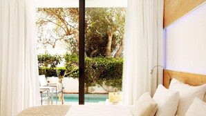 A bedroom with a large bed, white curtains, and a view of a swimming pool and greenery outside. - Monsuau Cala D'Or Hotel - Adults Only (Felanitx)