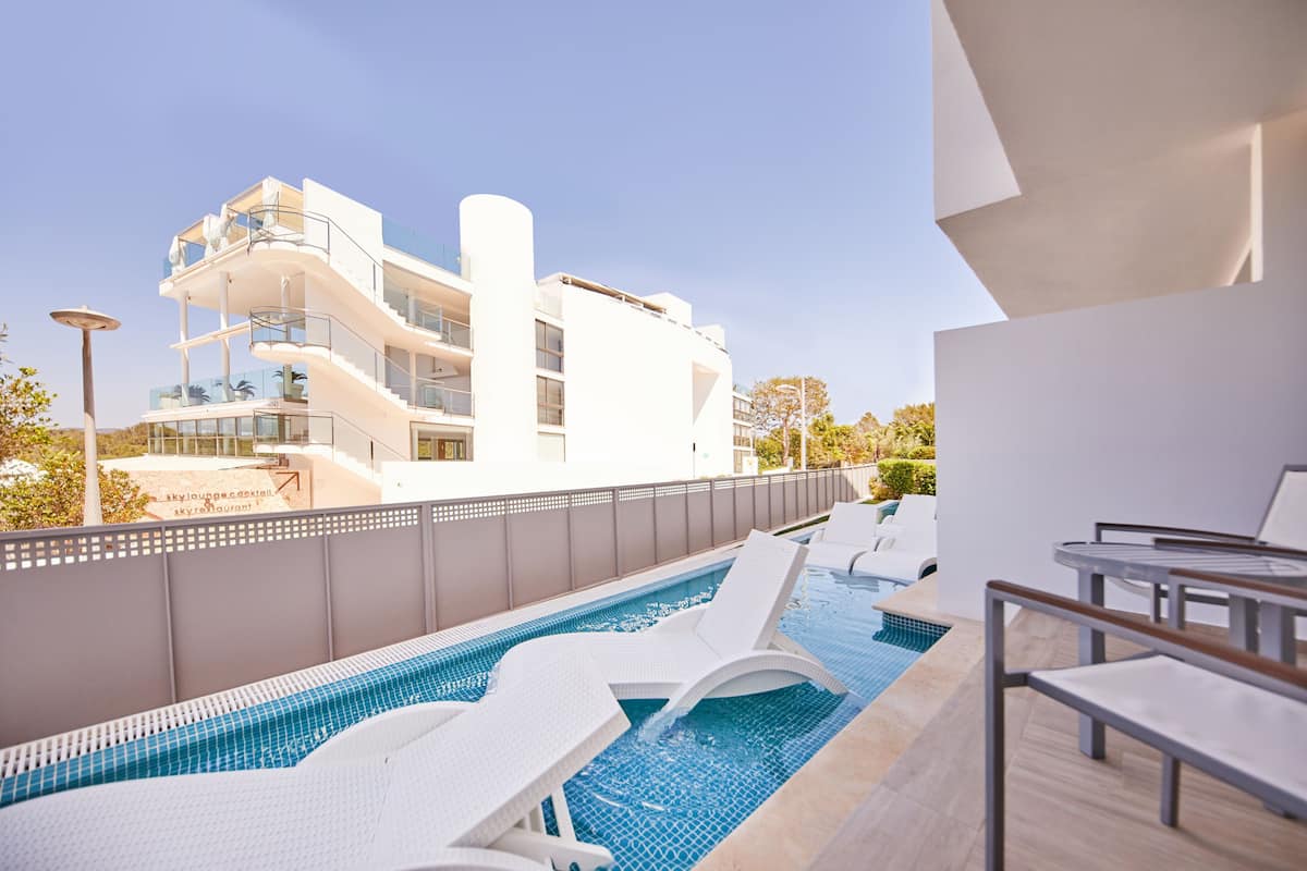 A pool area with lounge chairs, a modern building in the background, and a clear sky.