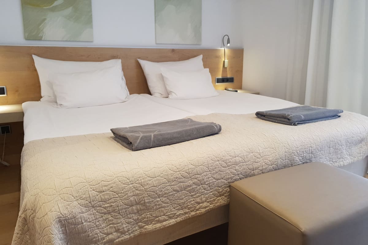 A hotel room with a large bed, two pillows, a bedside table, a lamp, and a folded towel on the bed.