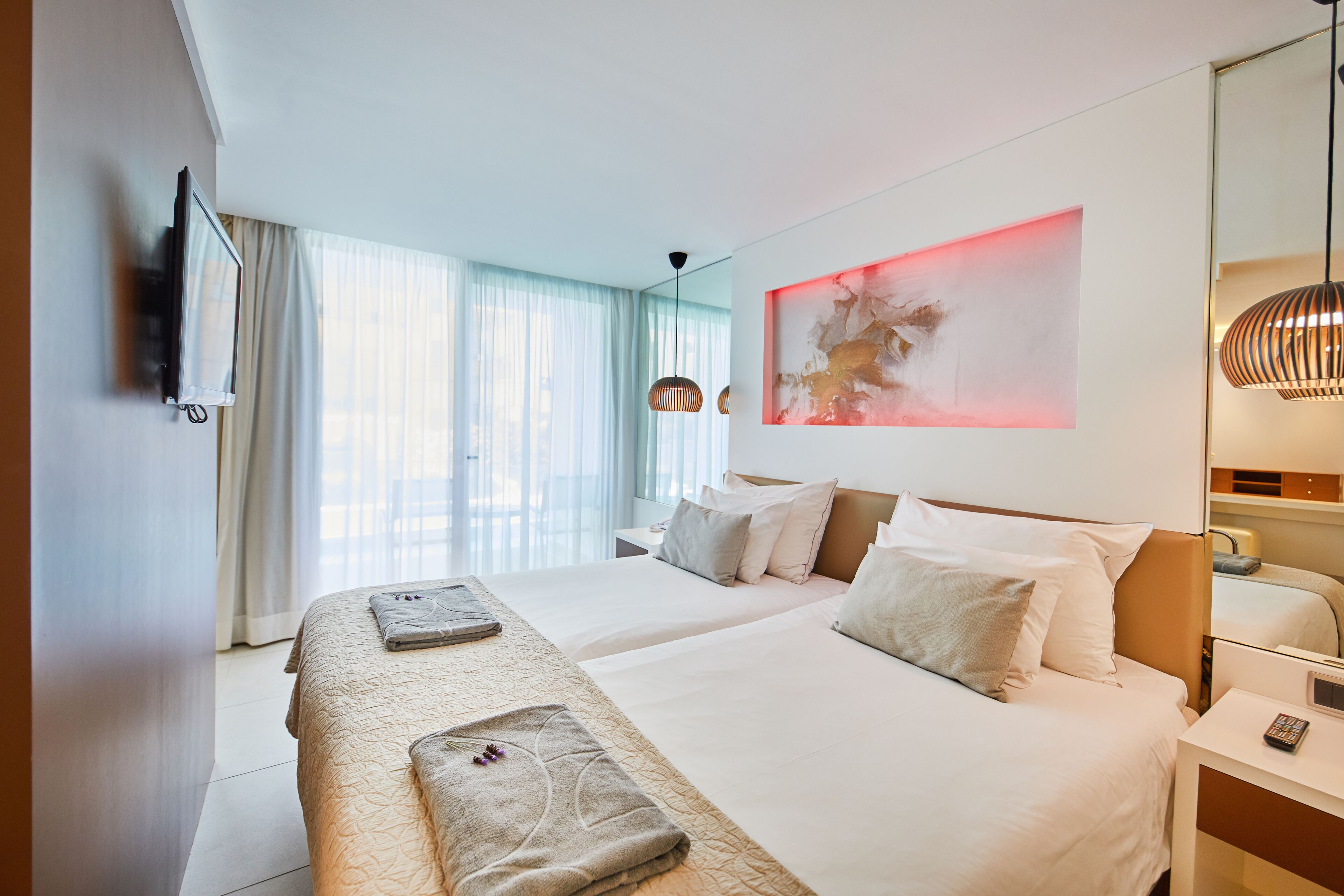 Une chambre d’hôtel avec deux lits, une télévision, un tableau et une table de chevet avec une lampe.