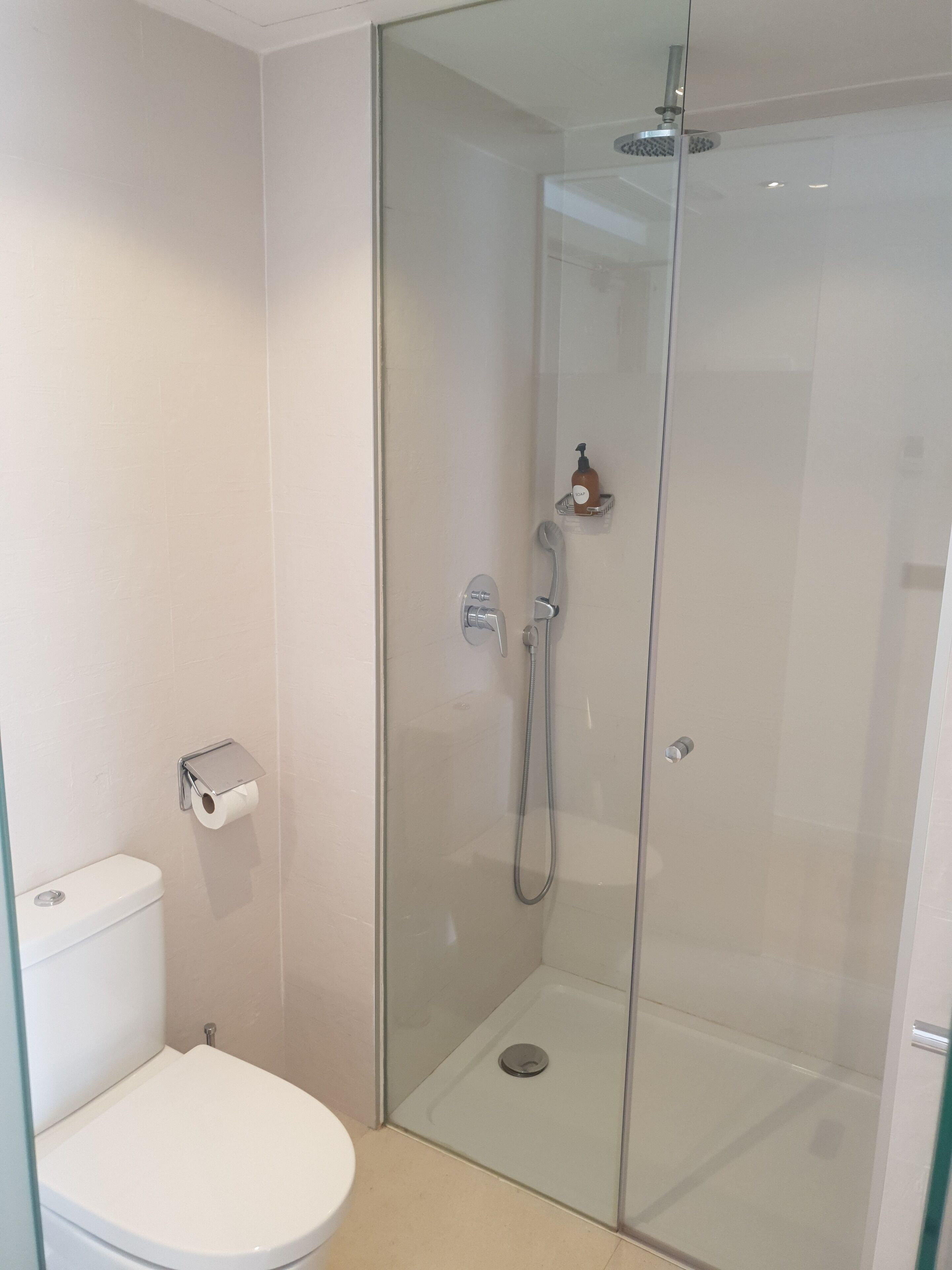 Une salle de bain moderne avec une douche à parois de verre, des toilettes et un distributeur de savon mural.