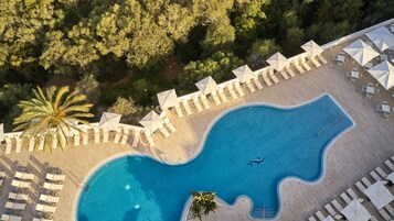 Vista aérea de un complejo turístico con piscina, sillas de descanso y sombrillas.