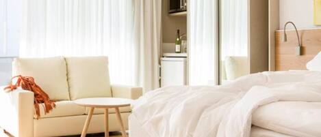 Una habitación de hotel con cama, una mesita redonda pequeña, un sofá y un minibar.