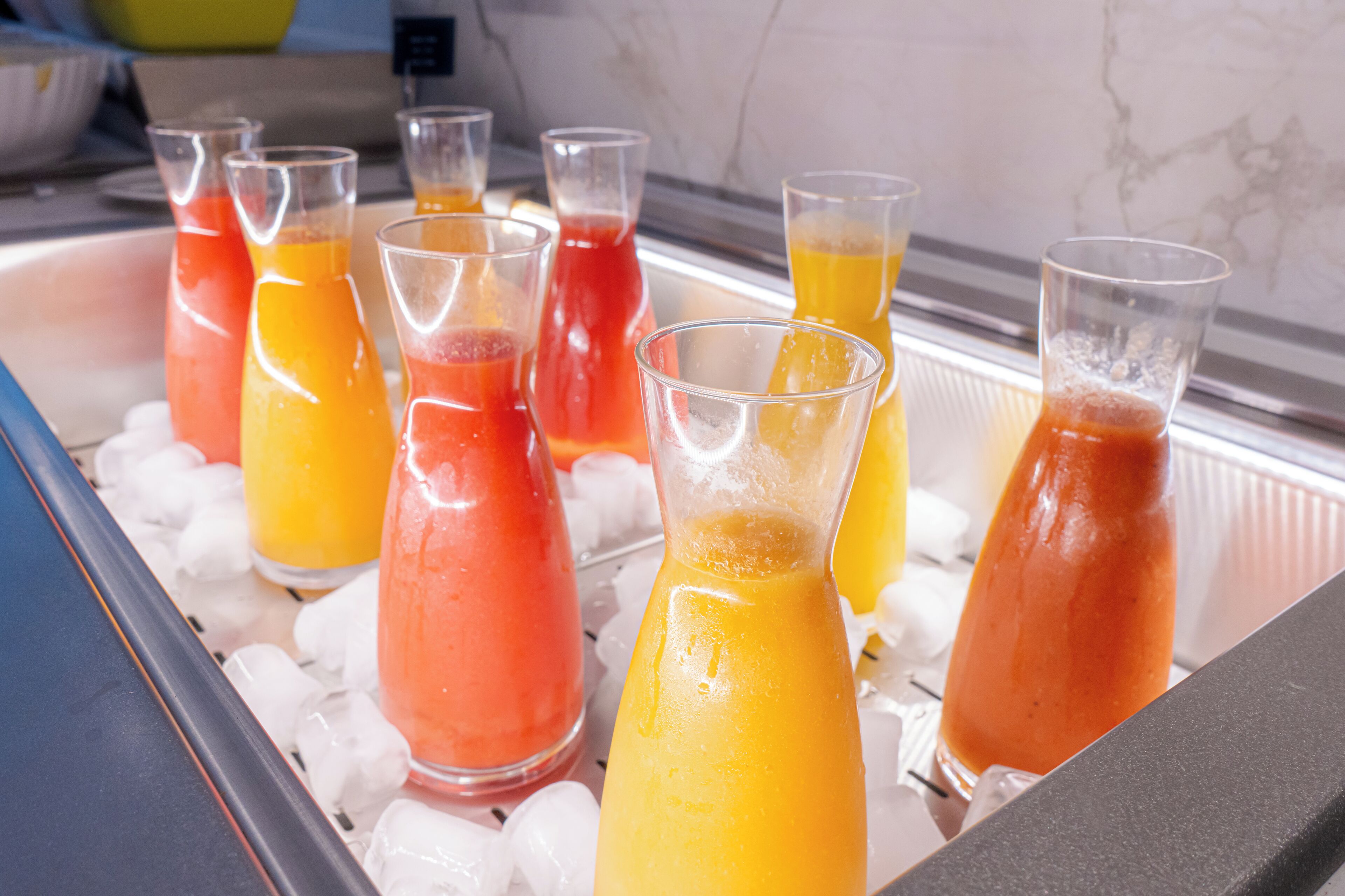 A beverage station with various drinks in glasses and bottles, surrounded by ice cubes.