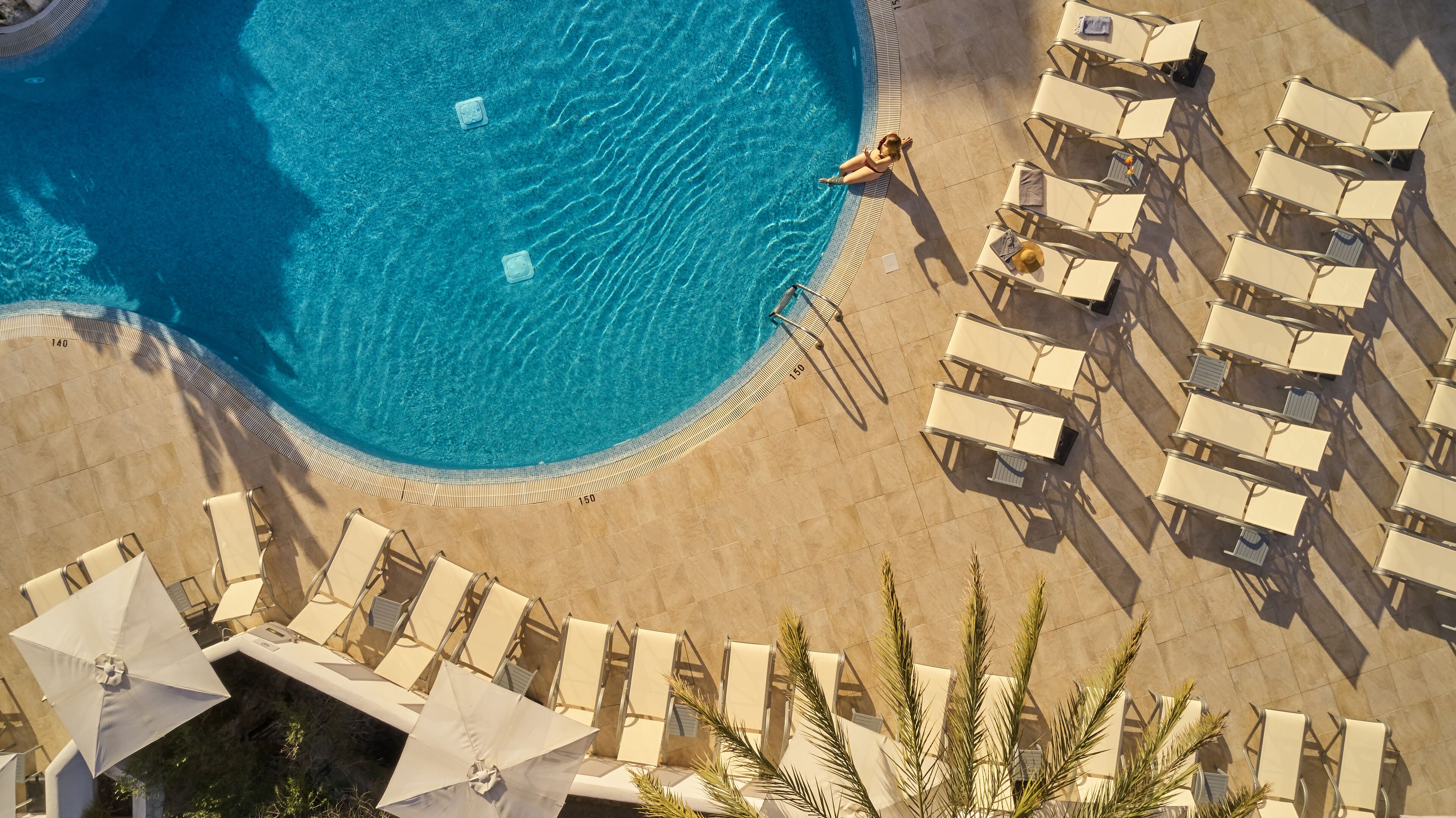An aerial view of a pool area with lounge chairs and umbrellas, surrounded by a tiled deck.