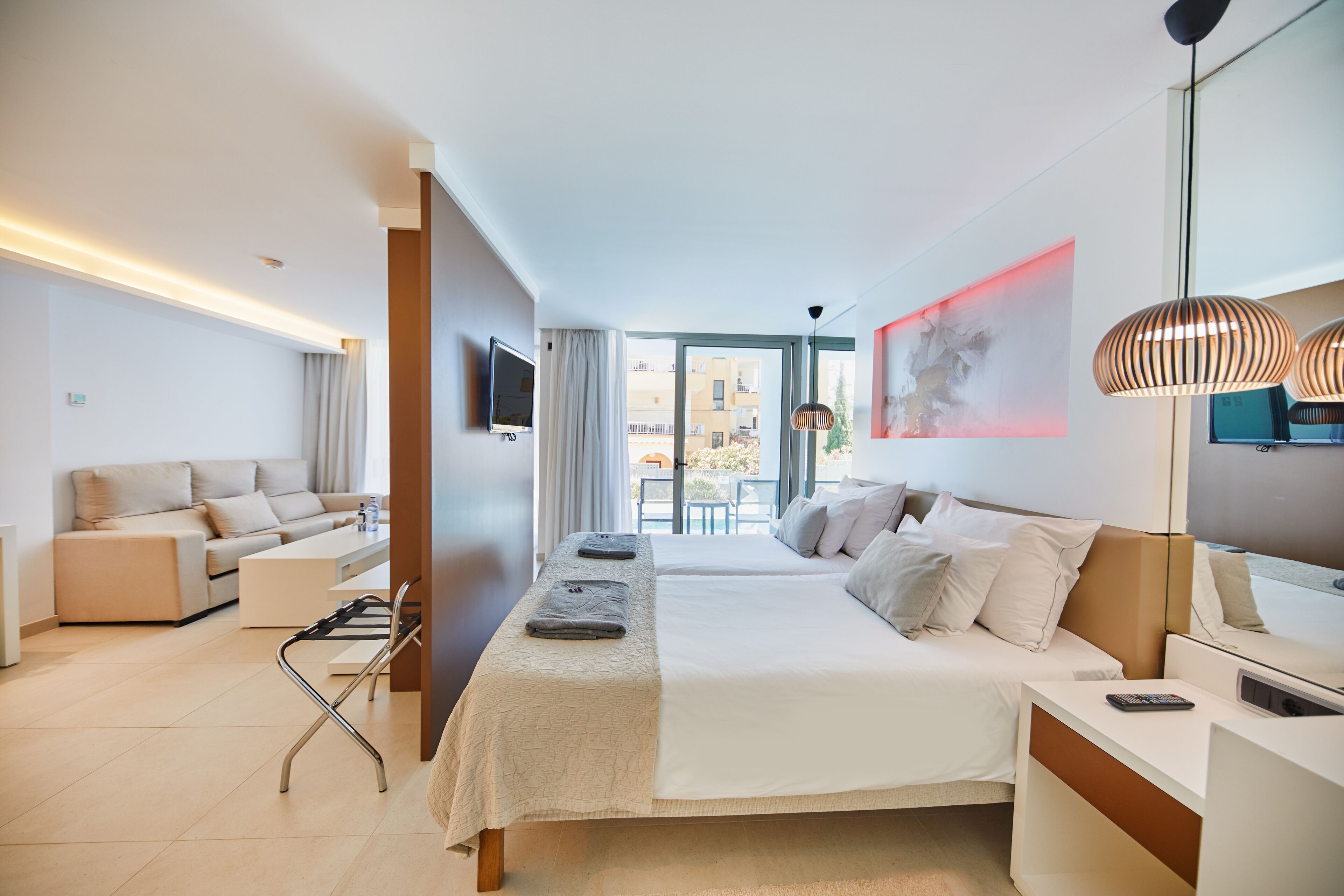 A modern hotel room with a large bed, a sofa, a desk, and a TV.