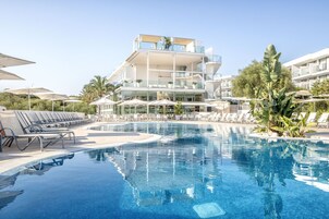 A modern hotel with a pool, sun loungers, and a clear blue sky.