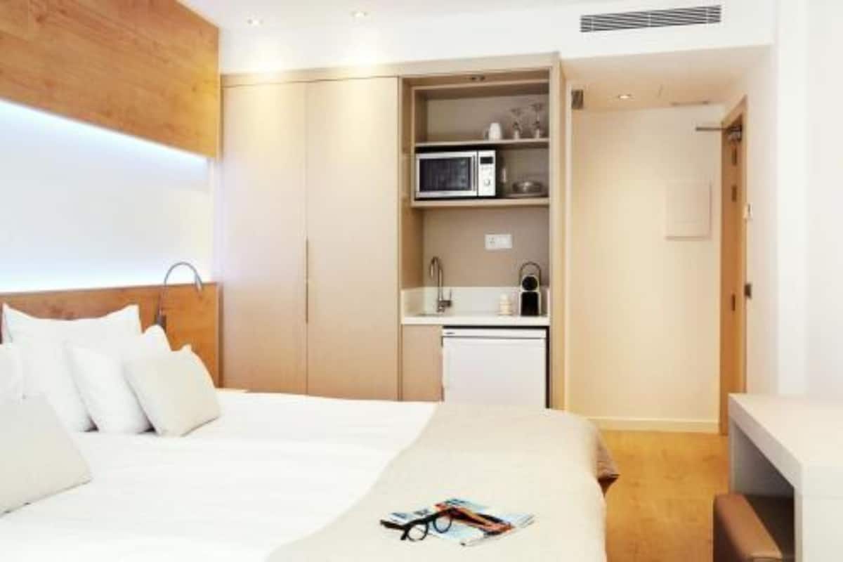 A modern hotel room with a bed, a small kitchenette, and a wooden accent wall.
