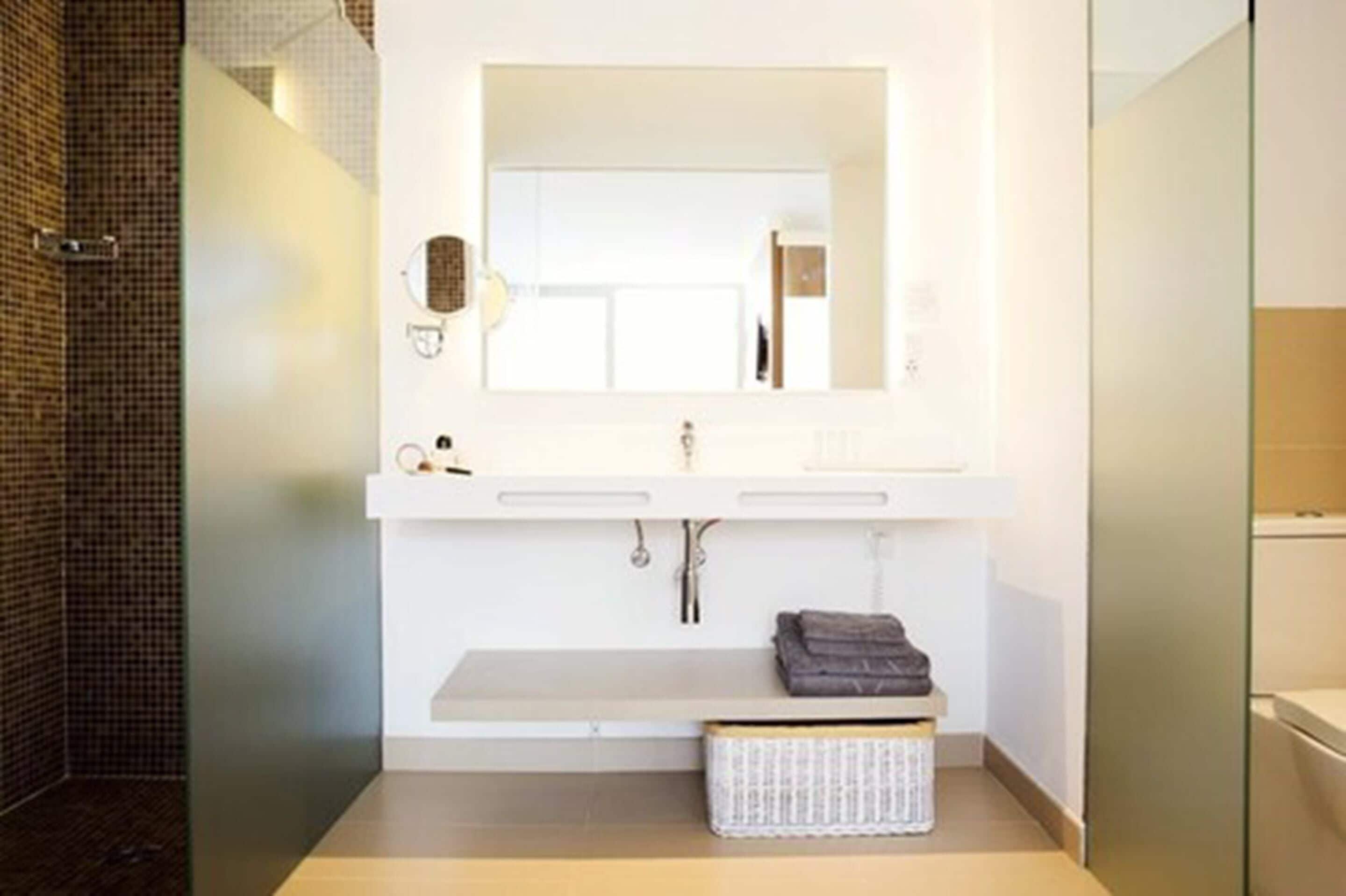 Un baño moderno con un espejo grande, tocador blanco y un perchero para toallas.