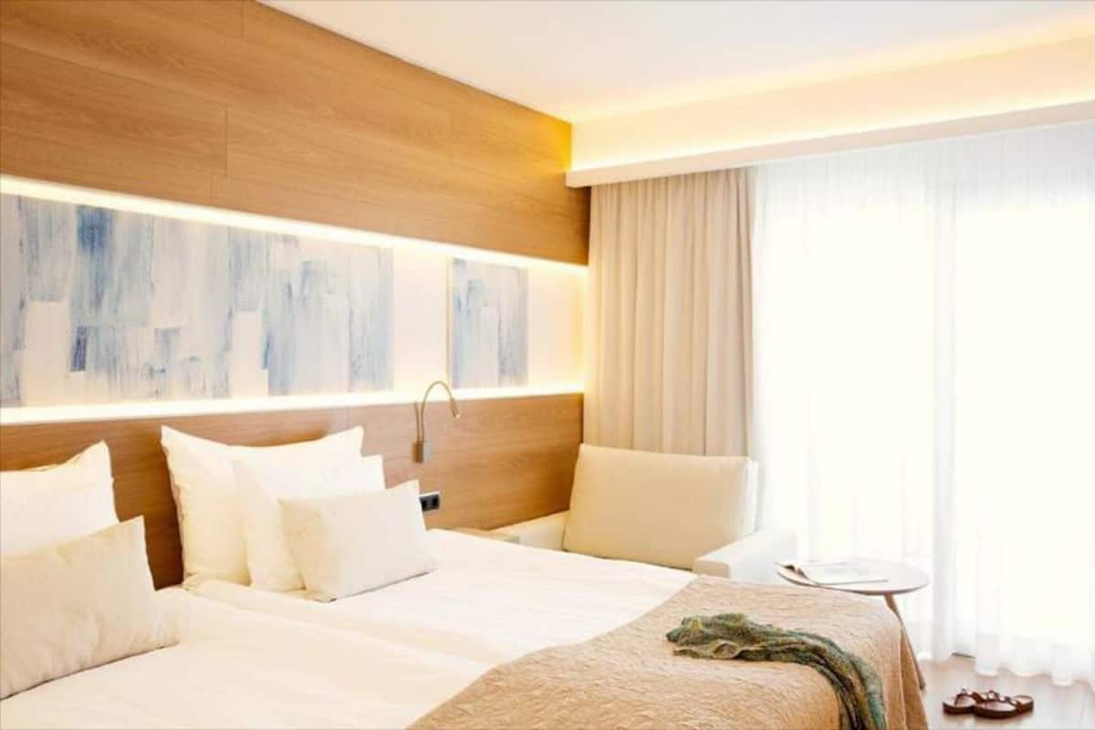 A hotel room with a large bed, a chair, a small table, and a window with curtains.