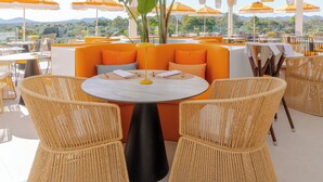 An outdoor seating area with wicker chairs, round tables, and orange umbrellas. - Monsuau Cala D'Or Hotel - Adults Only (Felanitx)