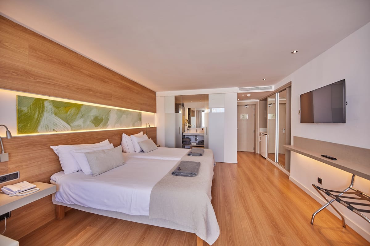 A modern hotel room with a wooden headboard, a large bed, a flat-screen TV, and a walk-in closet.