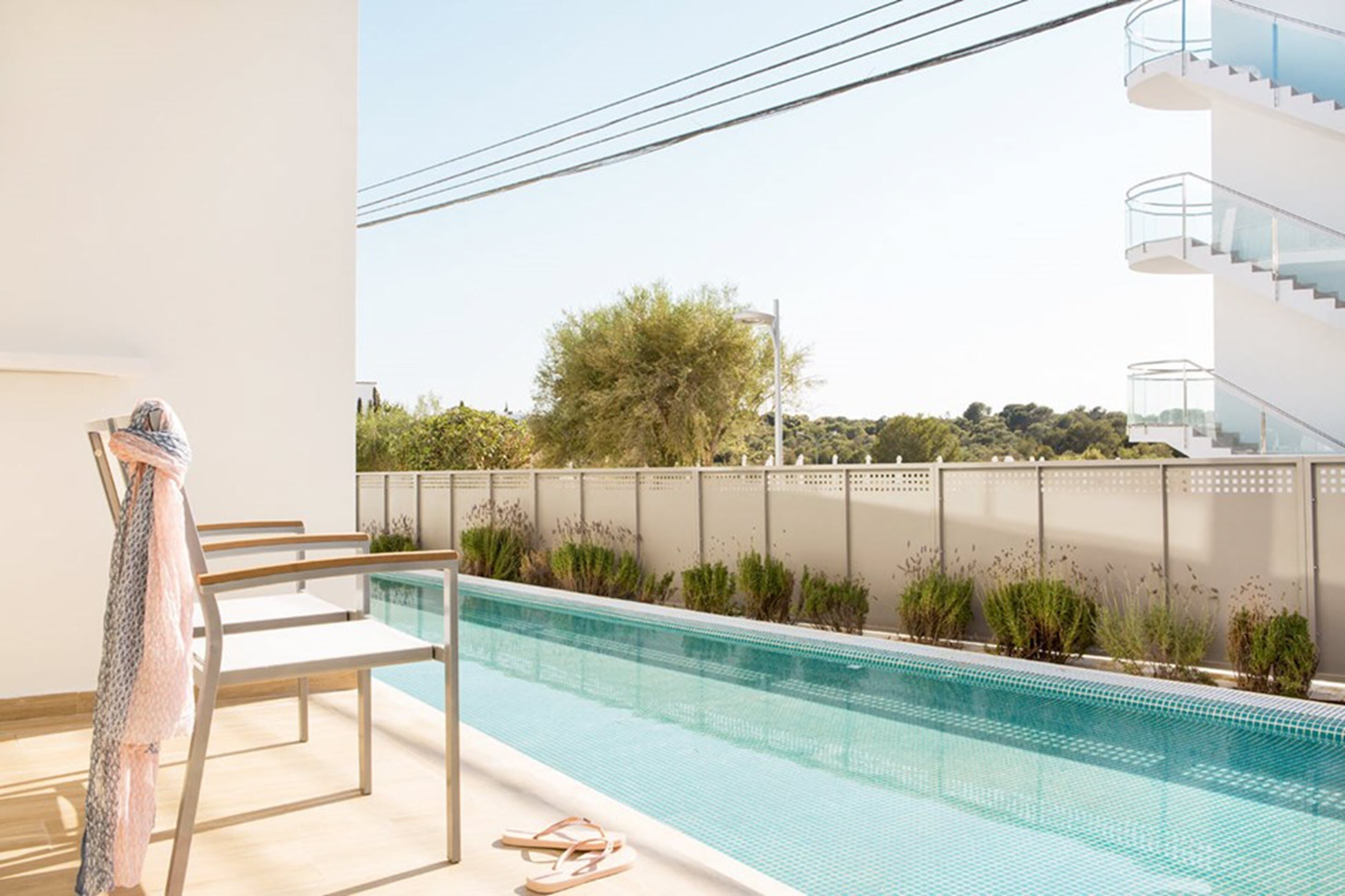 Un espace piscine extérieur moderne offrant une vue dégagée sur le paysage environnant, notamment sur un arbre et un bâtiment doté d’un balcon.