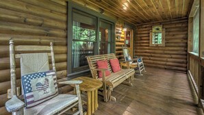 Eine Holzhütte mit Veranda, auf der ein Schaukelstuhl, eine Bank und ein Tisch stehen.