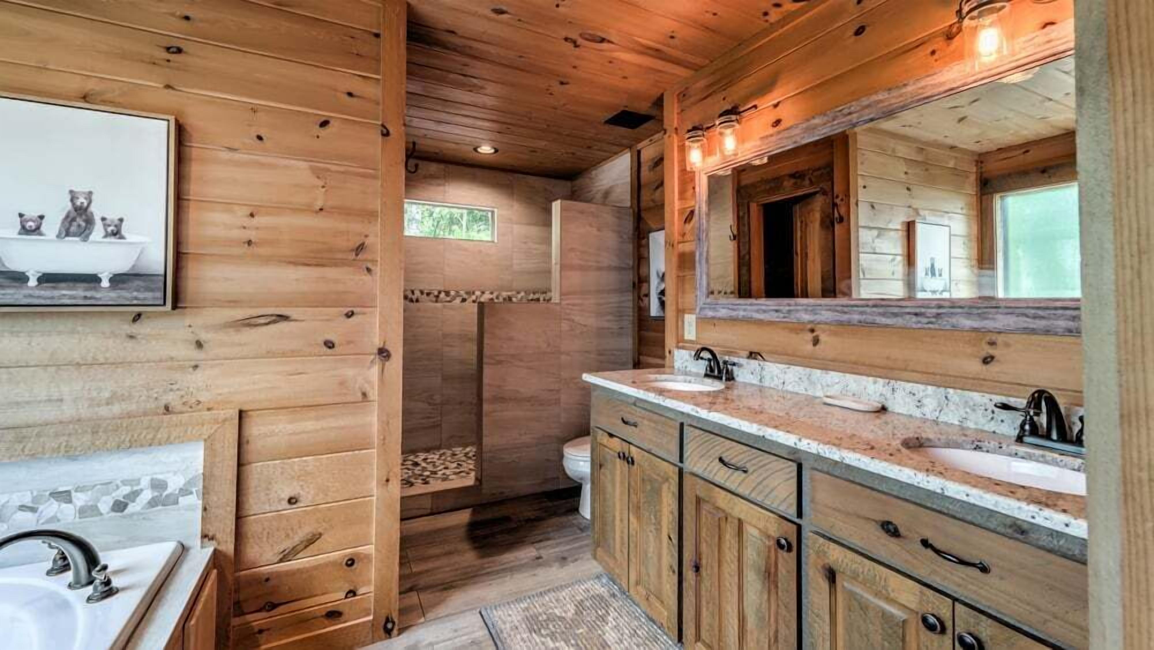 A wooden cabin bathroom with a large mirror, wooden cabinets, a bathtub, and a shower.