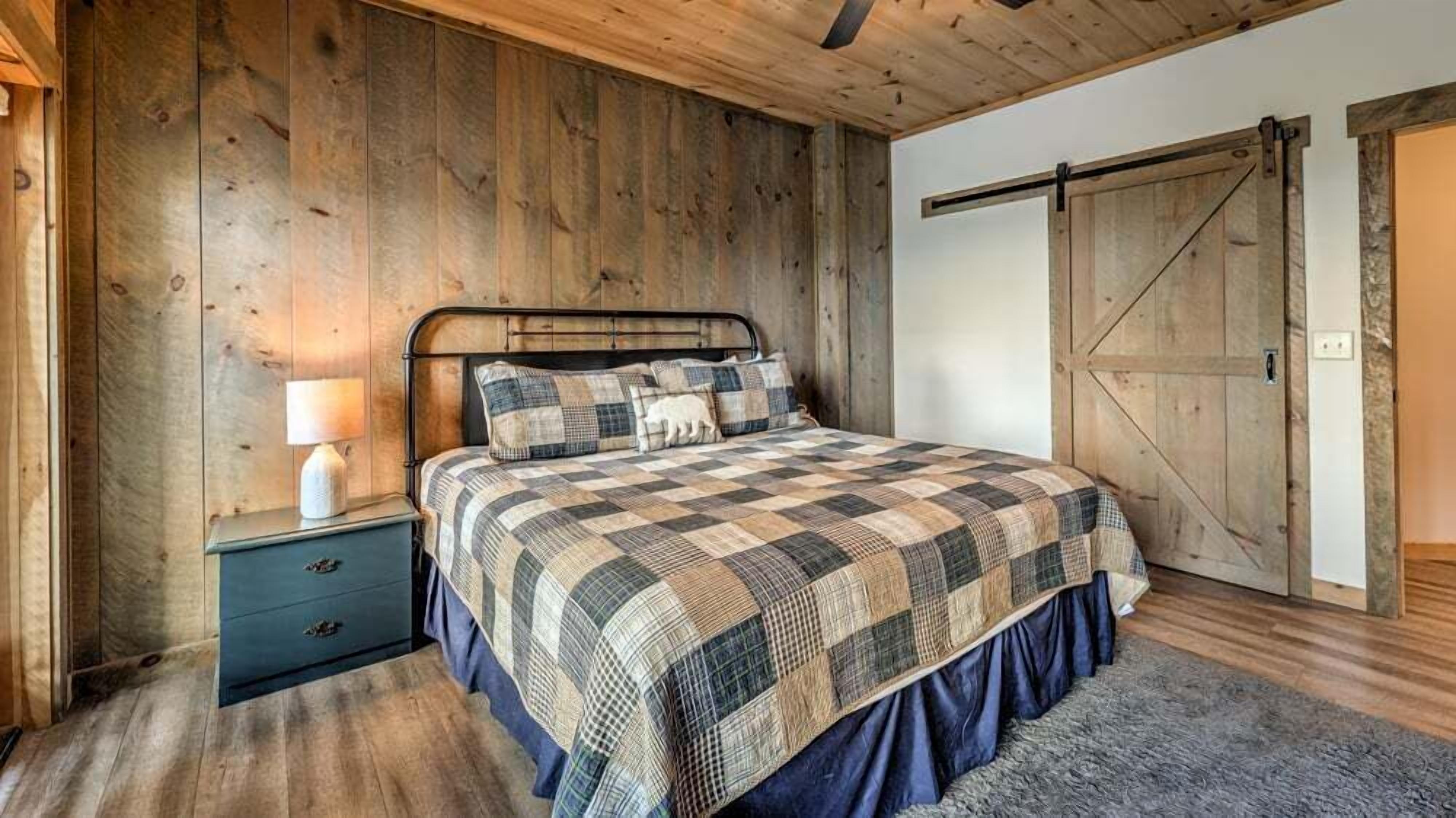Een slaapkamer met een houten vloer, een metalen bedframe, een gewatteerde spreidek en een nachtkastje met een lamp, plus een houten garderobe.