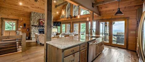 A spacious kitchen with a large island, wooden beams, and large windows offering views of the outdoors.