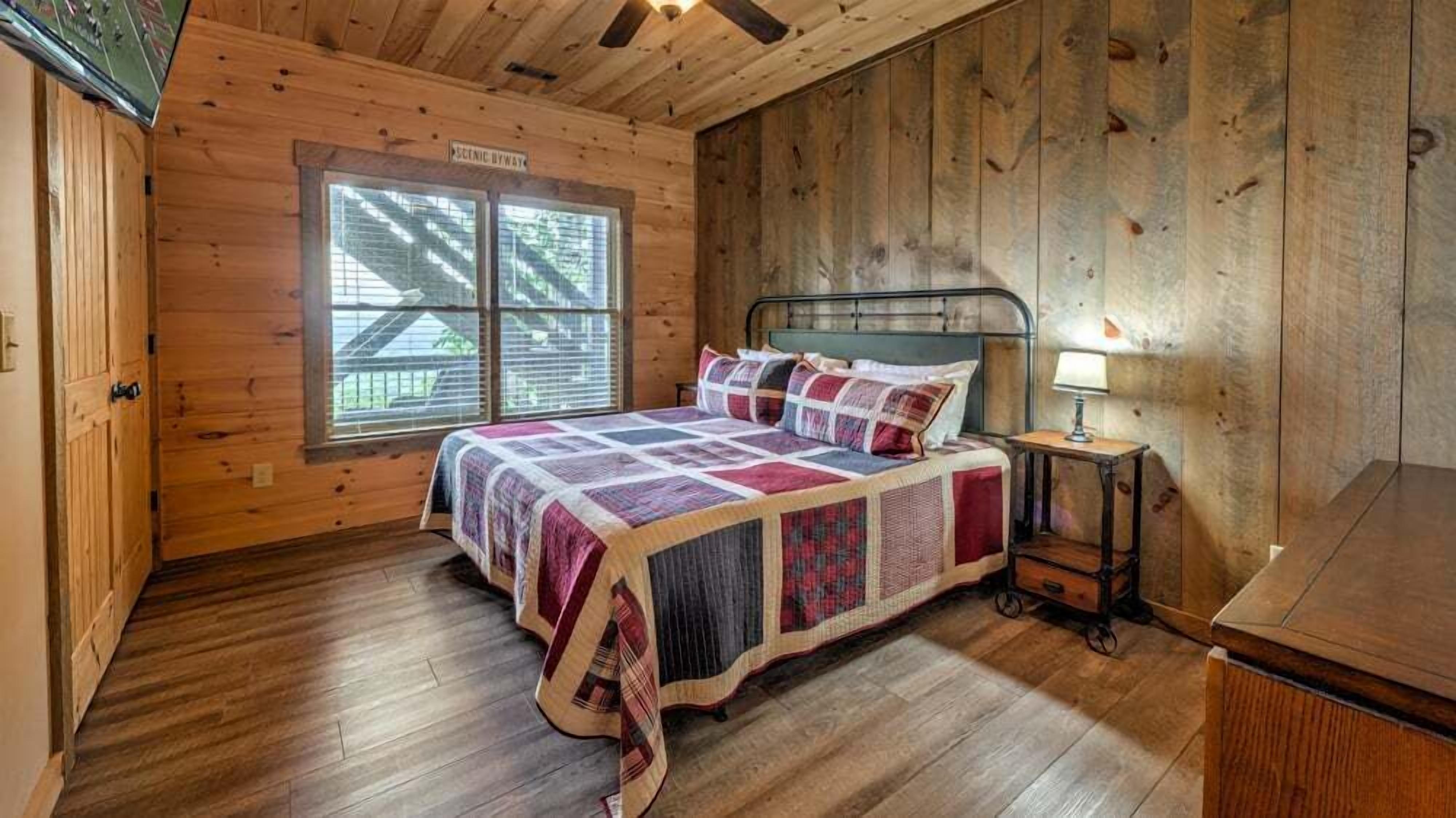 A wooden cabin bedroom with a bed, a nightstand, a lamp, and a window.